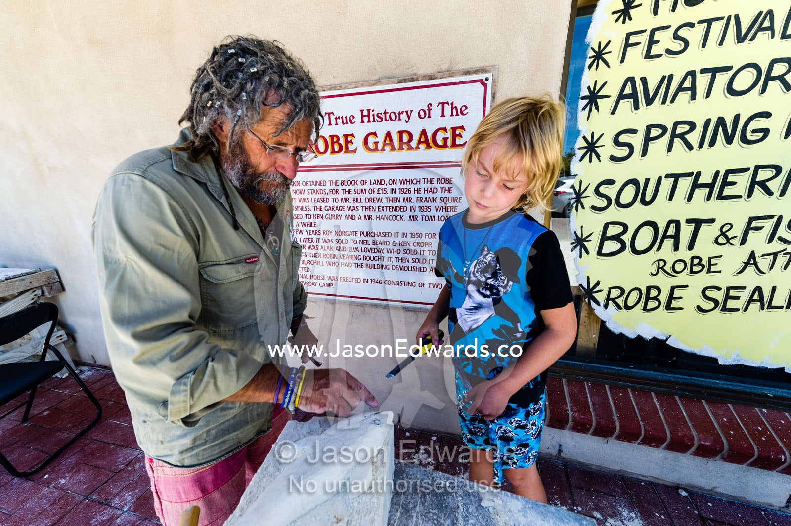 An artist helps a boy carve a shark into a block of sandstone during a school holiday program activity. Robe, Limestone Coast, South Australia, Australia.
