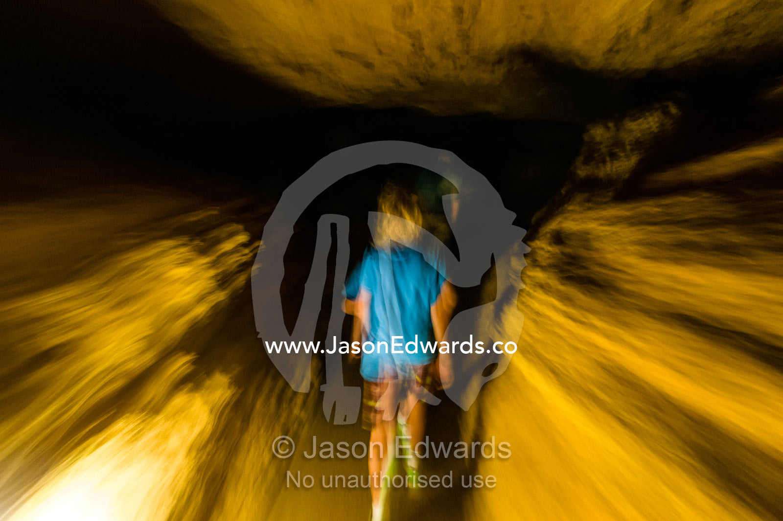 A boy walks through the darkness of a limestone cave tunnel. Naracoorte Caves National Park, South Australia, Australia.