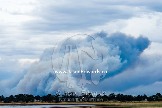 The billowing plume of smoke of a grassfire rises into the sky above farmland. Edenhope, Victoria, Australia.