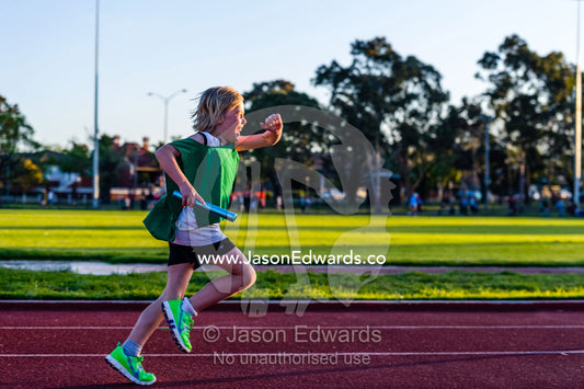 A laughing boy running in a baton relay on an athletics track. Collingwood, Melbourne, Victoria, Australia.