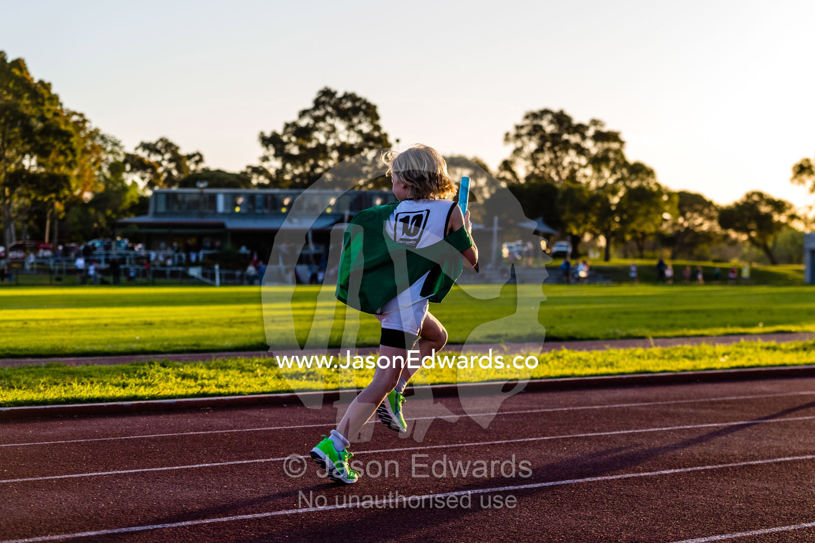 A laughing boy running in a baton relay on an athletics track. Collingwood, Melbourne, Victoria, Australia.