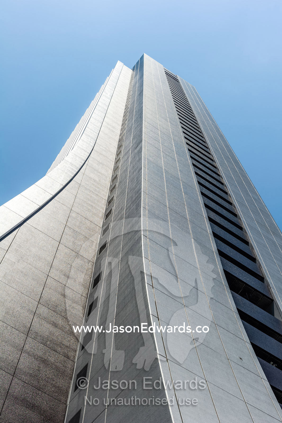 The linear steel facade of an office building in Tokyo towering into a blue sky. Shinjuku, Tokyo, Japan.