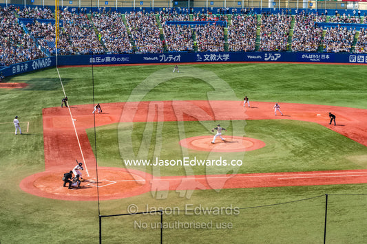 A large crowd watches a baseball match in Tokyo on a summer day. Meiji Jingu Stadium, Tokyo, Japan.