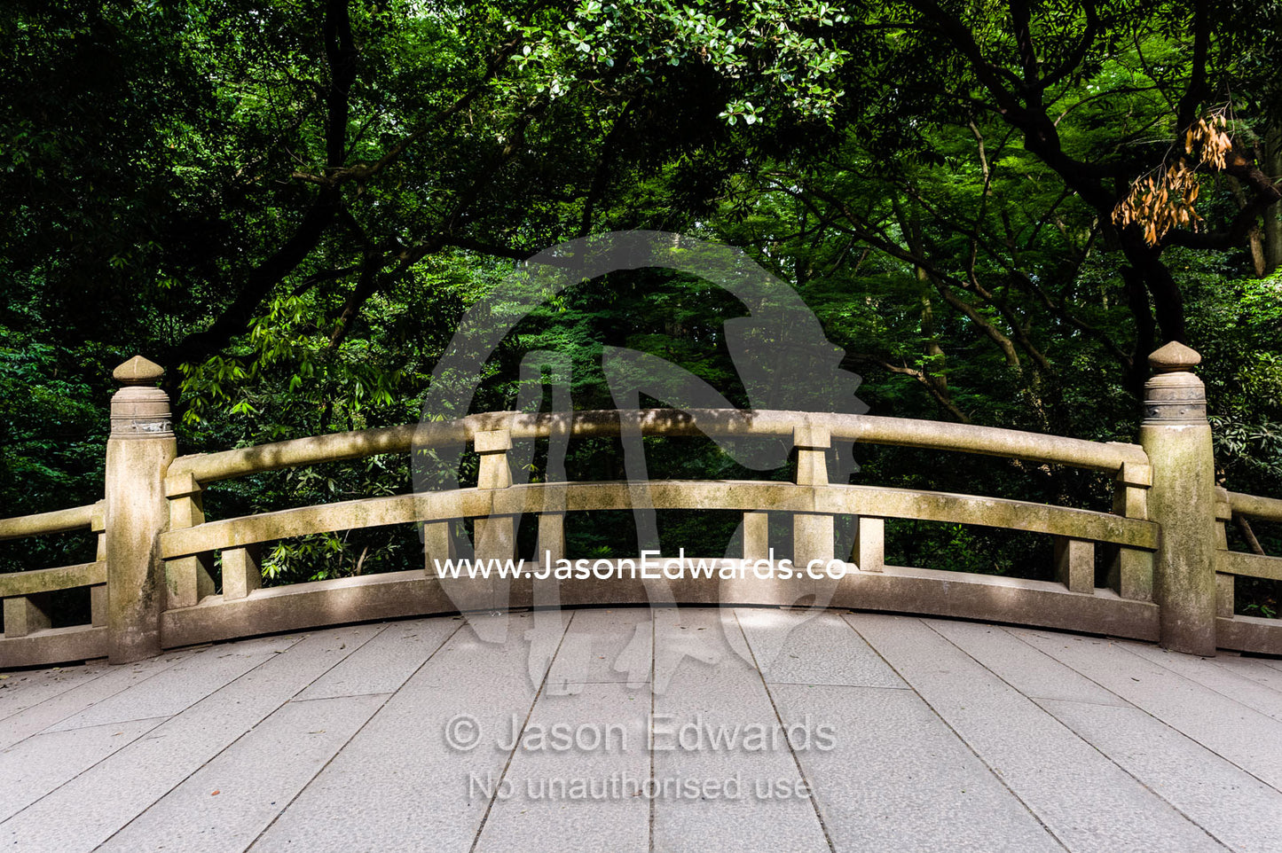 An arching bridge crossing a stream in a traditional Japanese garden. Meiji Shrine, Shinto Shrine, Shibuya, Tokyo, Japan.