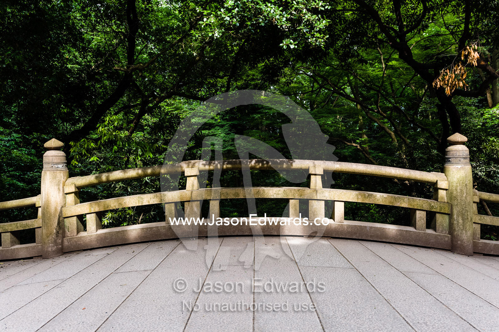 An arching bridge crossing a stream in a traditional Japanese garden. Meiji Shrine, Shinto Shrine, Shibuya, Tokyo, Japan.
