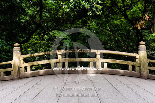 An arching bridge crossing a stream in a traditional Japanese garden. Meiji Shrine, Shinto Shrine, Shibuya, Tokyo, Japan.