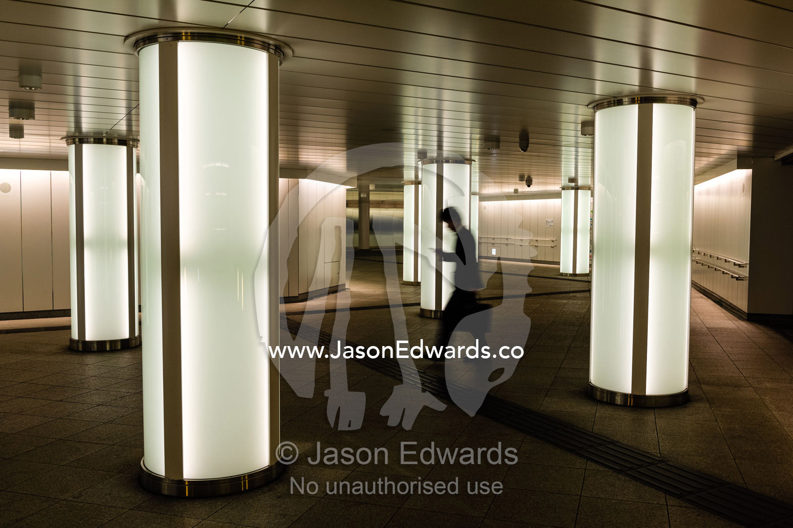 A salaryman checking his cell phone walking past light pillars in a subway. Shinjuku Station, Shinjuku, Tokyo, Japan.