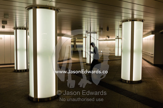 A salaryman checking his cell phone walking past light pillars in a subway. Shinjuku Station, Shinjuku, Tokyo, Japan.