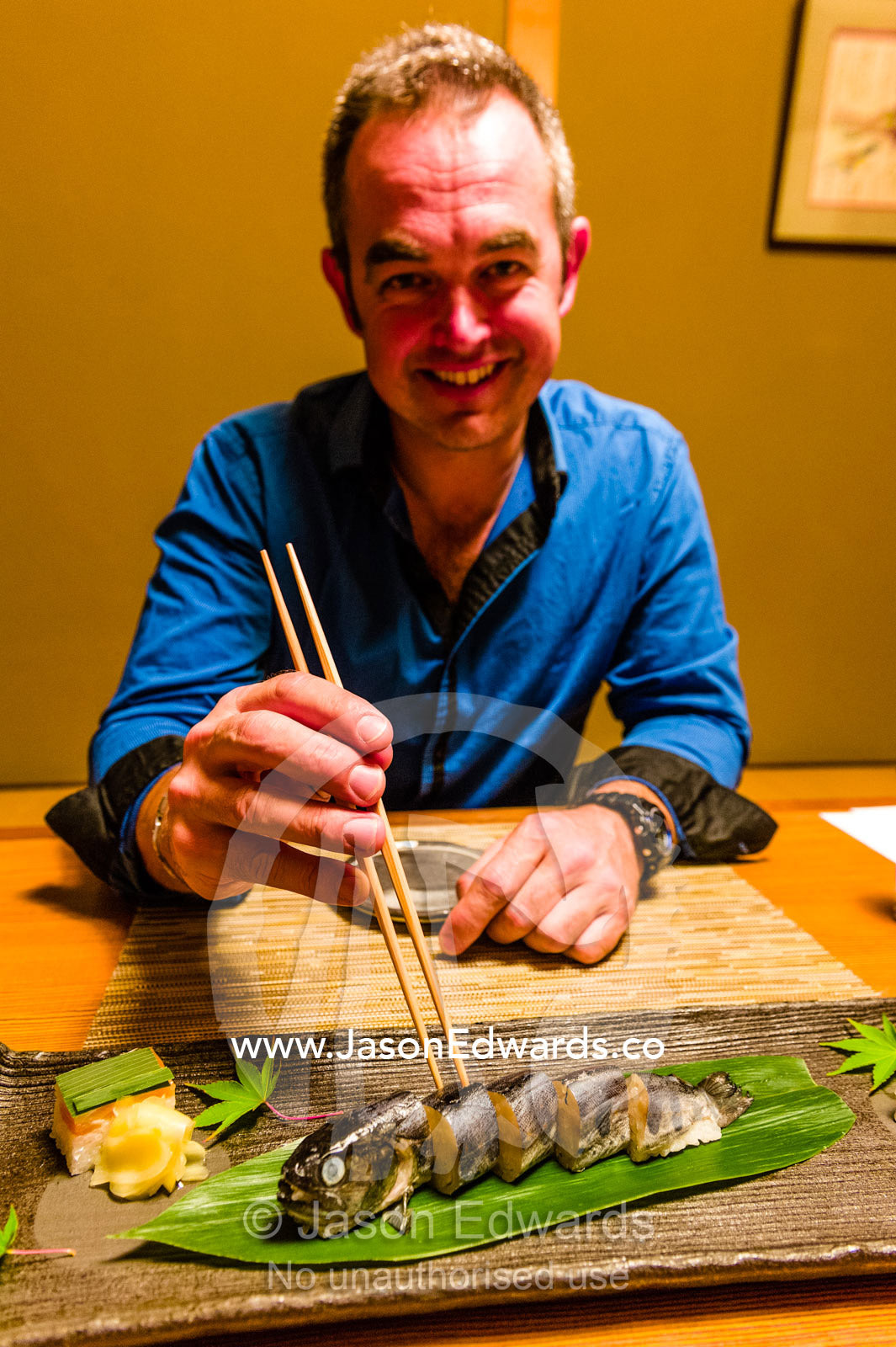 A man using chopsticks to eat a river fish called Ayu stuffed with rice is called Ayu Mesi served at Kaiseki, a traditional multi-course Japanese dinner. Unryu Onsen, Izu Peninsula, Shizuoka Prefecture, Japan.