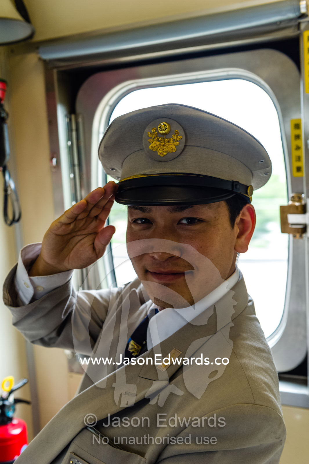 A train conductor in a pressed uniform salutes. Nagoya, Chubu Region, Japan.