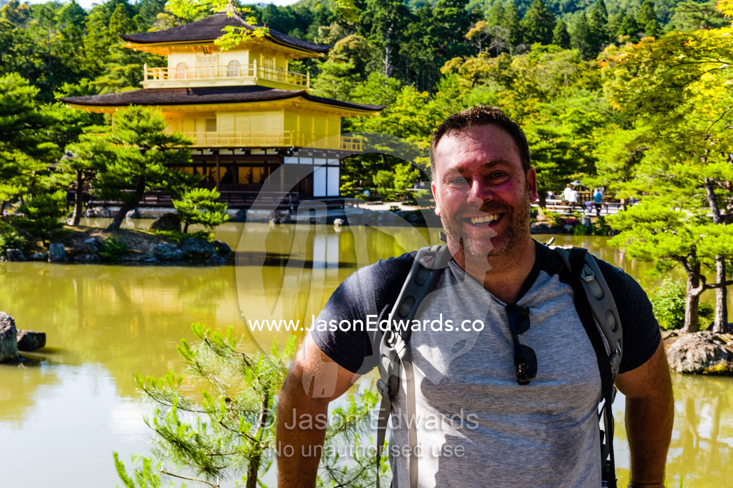 A tourist standing in front of the Temple of the Golden Pavilion on the shore of an ornamental lake. Temple of the Golden Pavilion, Kinkaku-ji, Kyoto, Japan.