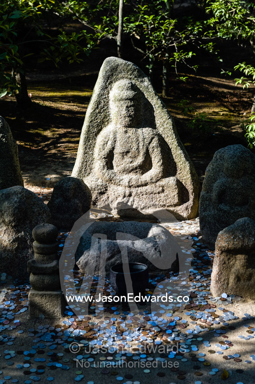 People throw coins at a statue of Buddha near the Temple of the Golden Pavilion. Temple of the Golden Pavilion, Kinkaku-ji, Kyoto, Japan.