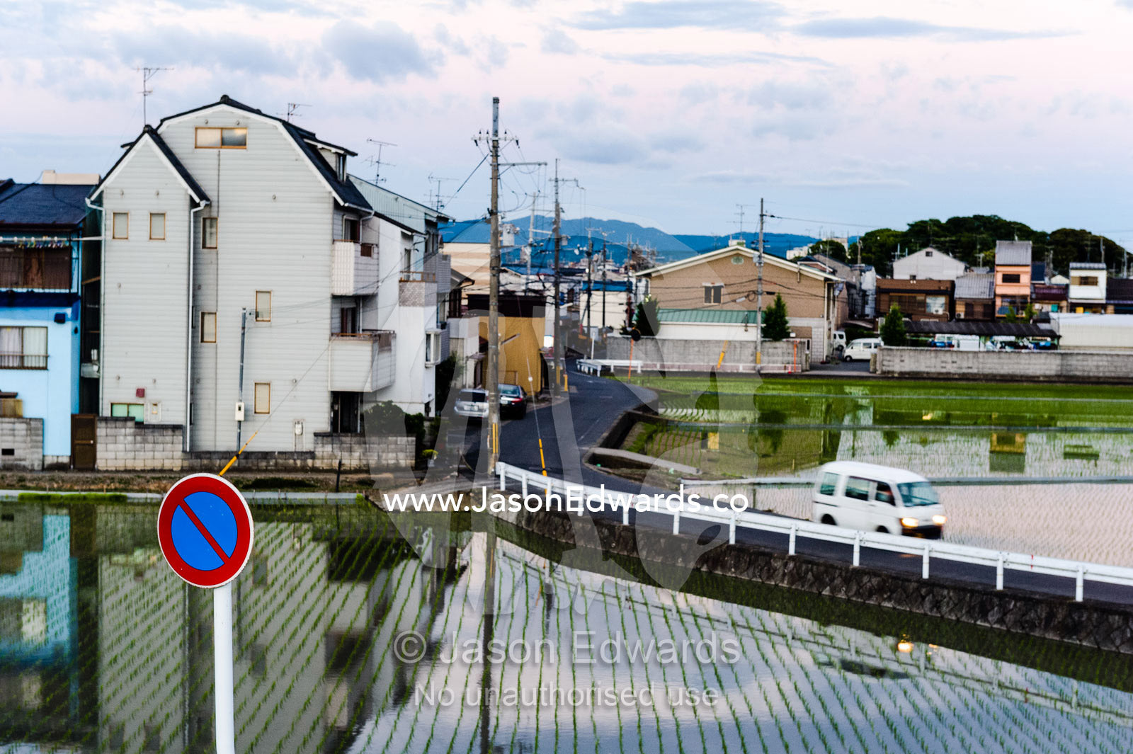 A road passes between houses and rice paddy's in a Japanese suburb. Arashiyama Bamboo Grove, Arashiyama District, Kyoto, Japan.