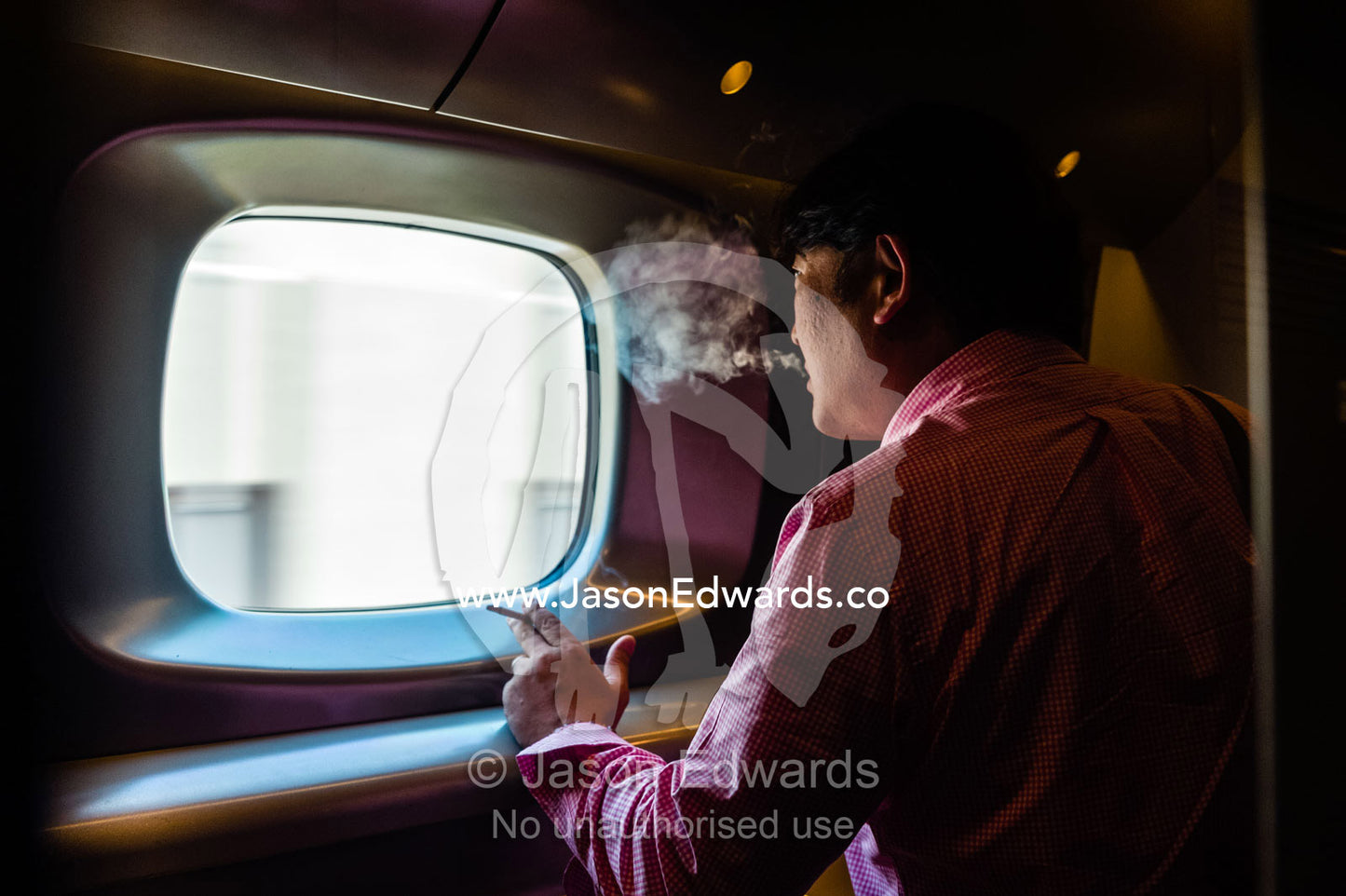 A businessman smoking a cigarette in the smoking compartment of a bullet train. Hiroshima, Honshu Island, Japan.