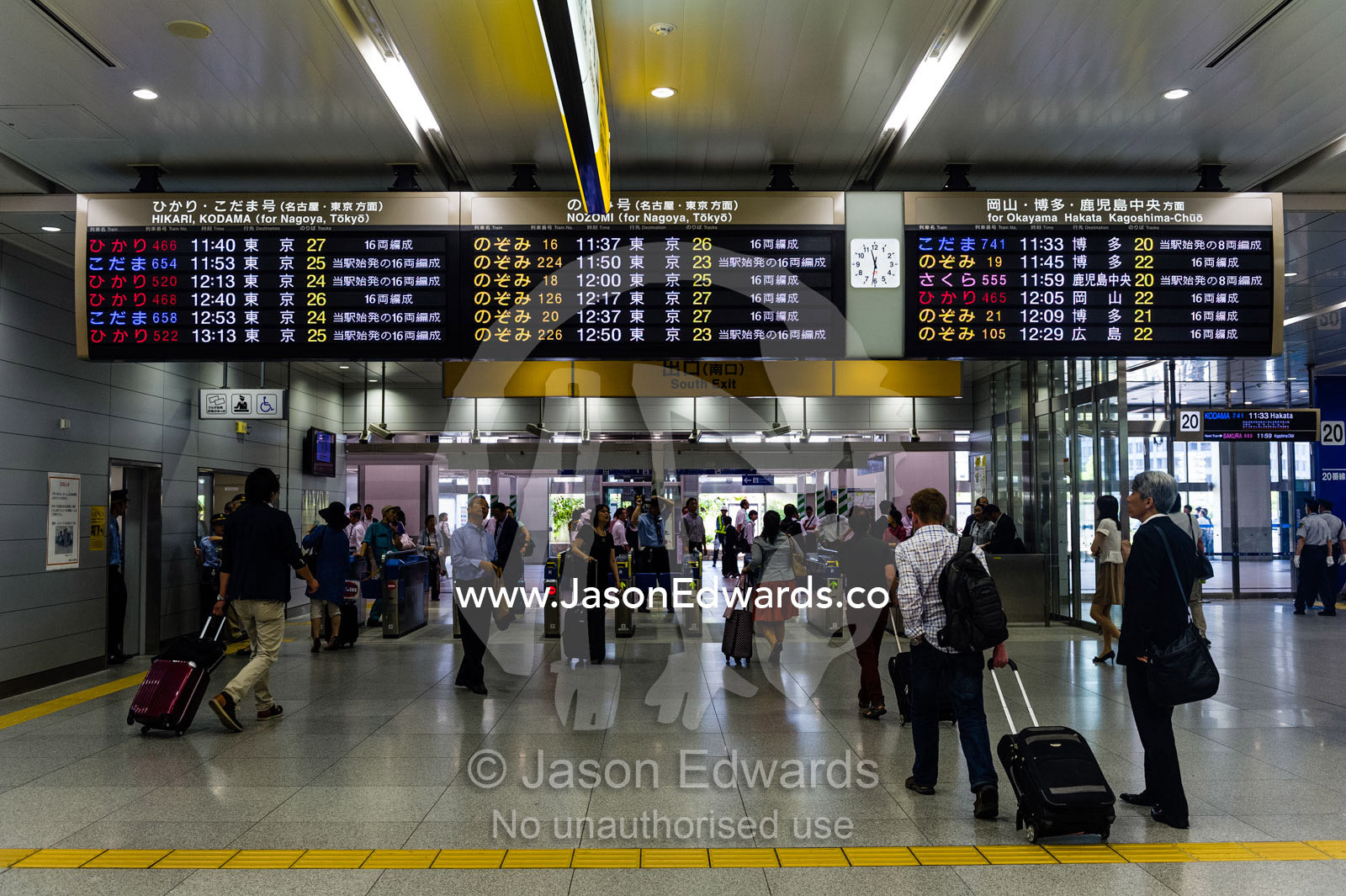 Commuters walking beneath a departure and arrival schedule at a railway station. Shinjuku Station, Shinjuku, Tokyo, Japan.
