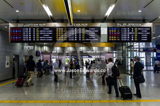 Commuters walking beneath a departure and arrival schedule at a railway station. Shinjuku Station, Shinjuku, Tokyo, Japan.