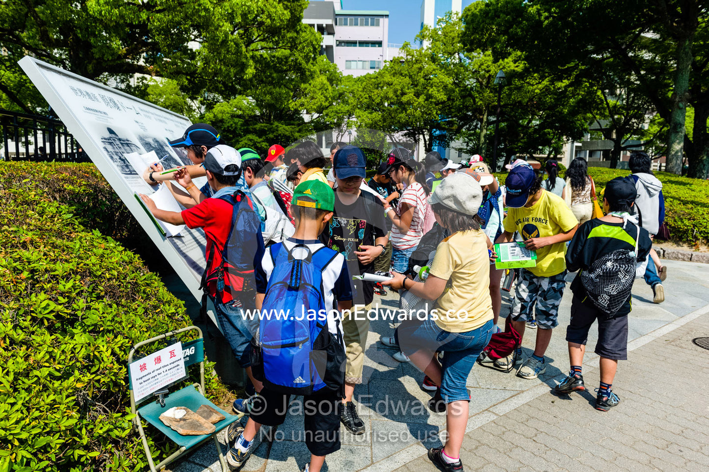Japanese school children study a sign at the ruin of the Hiroshima Prefectural Industrial Promotion Hall known as the Atomic Bomb Dome or Genbaku Domu. Hiroshima Peace Memorial Park, Hiroshima, Honshu Island, Japan.