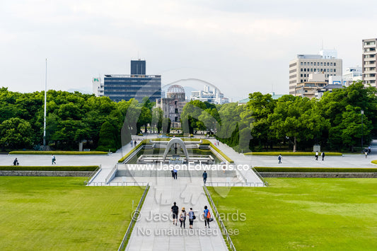 A saddle-shaped monument covers a cenotaph holding the names of all of the people killed by the bomb. The monument frames the Peace Flame and the A-Bomb Dome. Hiroshima Peace Memorial Park, Hiroshima, Honshu Island, Japan.