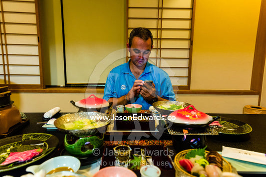 A man texting on his cell phone during Kaiseki a traditional multi-course Japanese dinner. Miyajima, Itsukushima Island, Inland Sea of Japan, Hiroshima Bay, Japan.