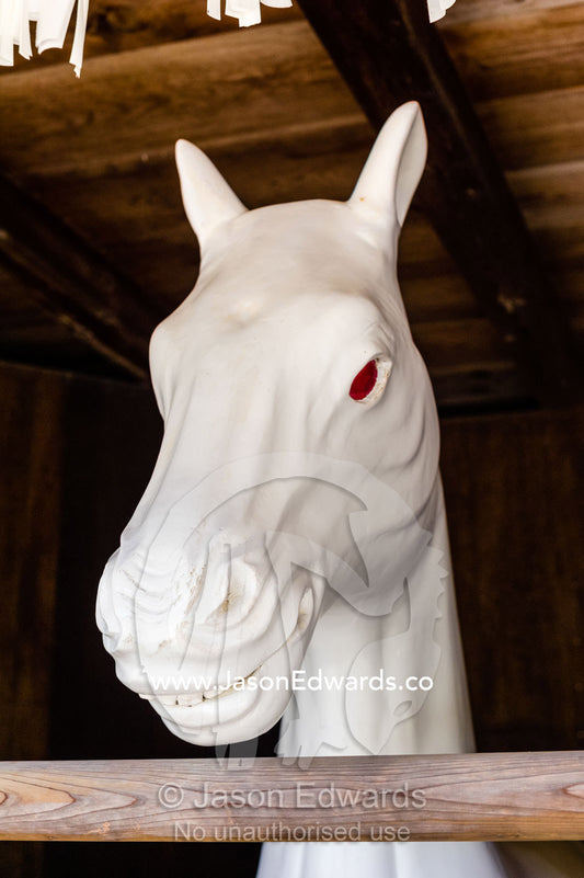 A statue of a white horse with fiery red eyes in a stable at a shrine. Itsukushima Shrine, Miyajima, Itsukushima Island, Inland Sea of Japan, Hiroshima Bay, Japan.