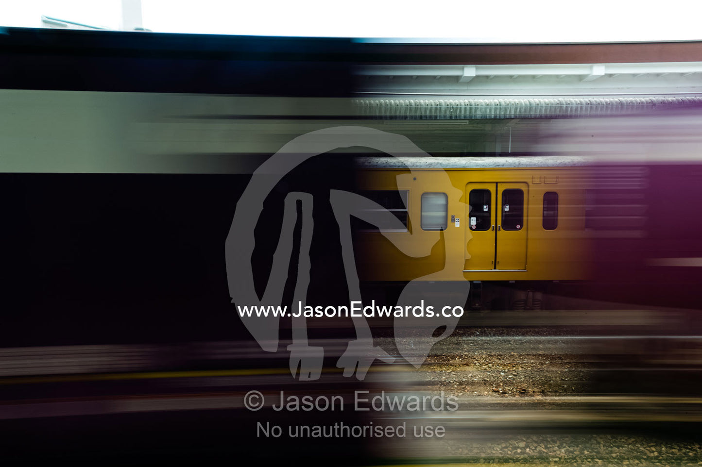 A speeding train passes an old yellow commuter train parked at a railway platform in Japan. Atami Station, Atami, Shizuoka, Japan.