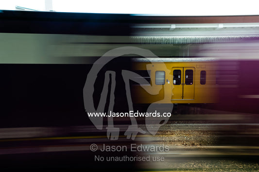 A speeding train passes an old yellow commuter train parked at a railway platform in Japan. Atami Station, Atami, Shizuoka, Japan.