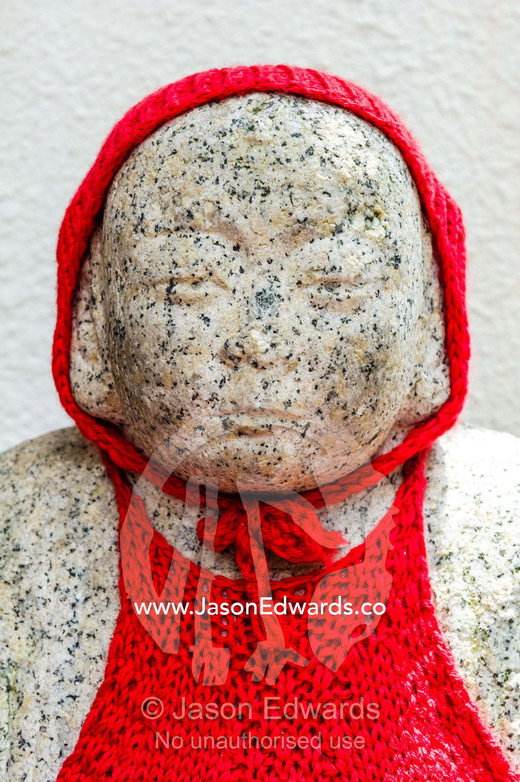 A red hood on a Hibaku Jizo statue in a small cemetery adjacent to the Atomic Bomb Dome where the stone on the tombstones was fused by the blast. Hiroshima Peace Memorial Park, Hiroshima, Honshu Island, Japan.