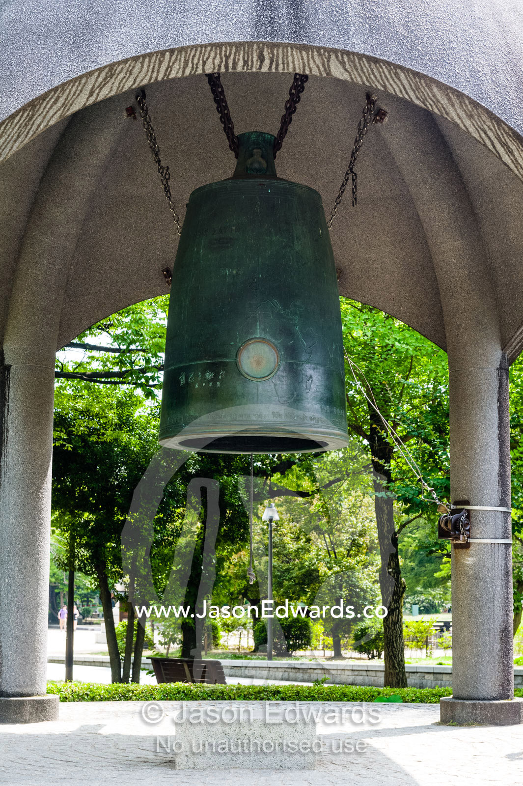 A large Japanese peace bell hanging inside a small open-sided structure. Visitors are encouraged to ring the bell for world peace. Hiroshima Peace Memorial Park, Hiroshima, Honshu Island, Japan.