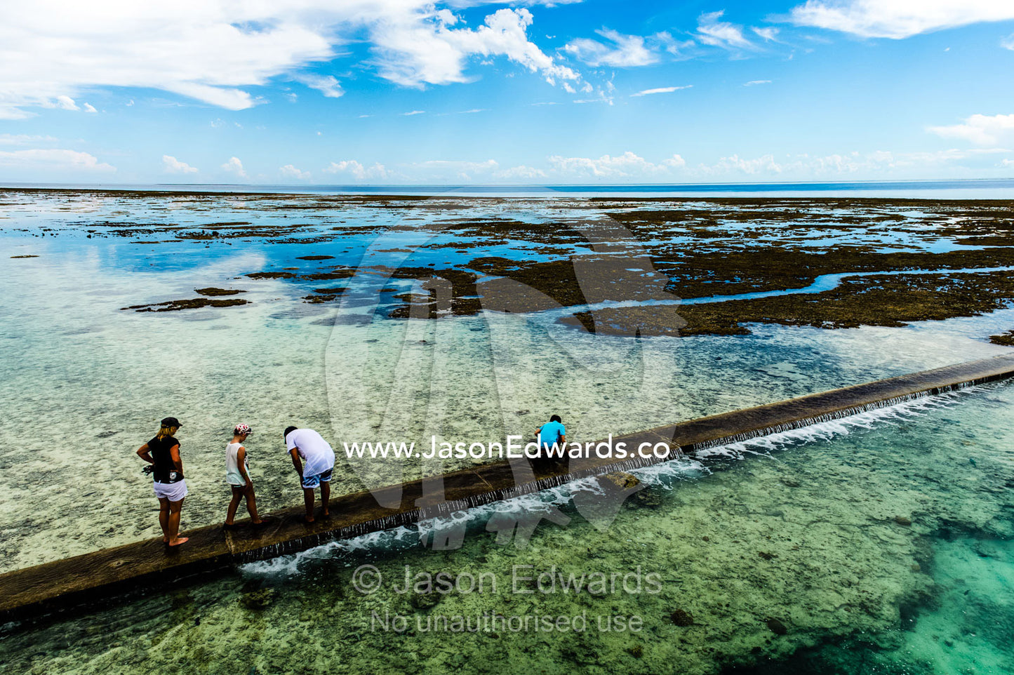 Tourists walk along a harbour retaining wall at low tide. Wreck Beach, Heron Island, Great Barrier Reef, Queensland, Australia.