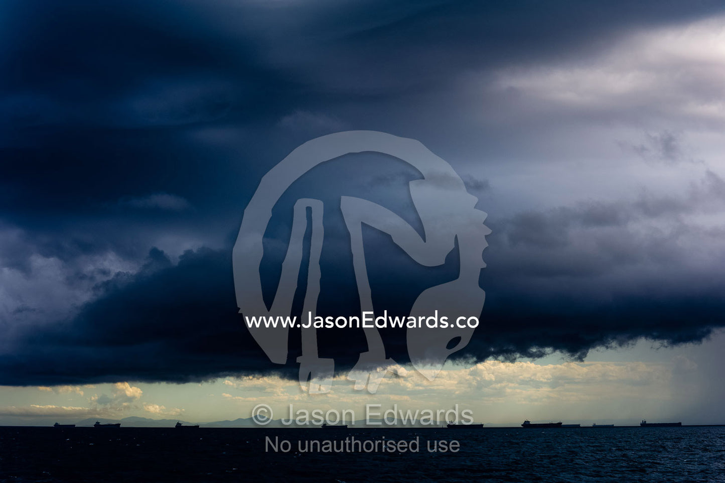 A menacing tropical rainstorm darkens the ocean and sky over cargo ships at anchor. Gladstone, Queensland, Australia.