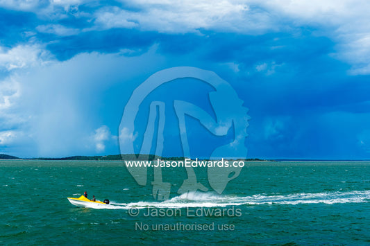 A small speed boat races across the ocean ahead of a storm. Gladstone, Queensland, Australia.