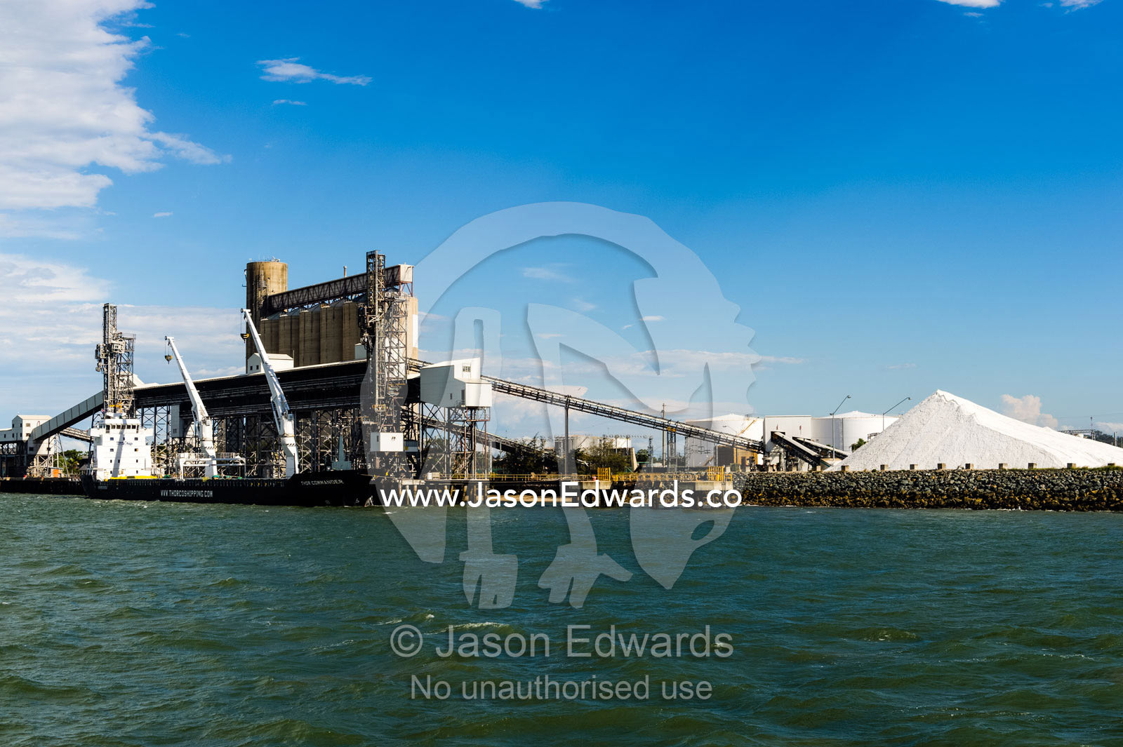 A project type ship loading wheat or bulk cargo. The stockpile of white material is calcite, used in industrial manufacturing, including toothpaste. Gladstone, Queensland, Australia.