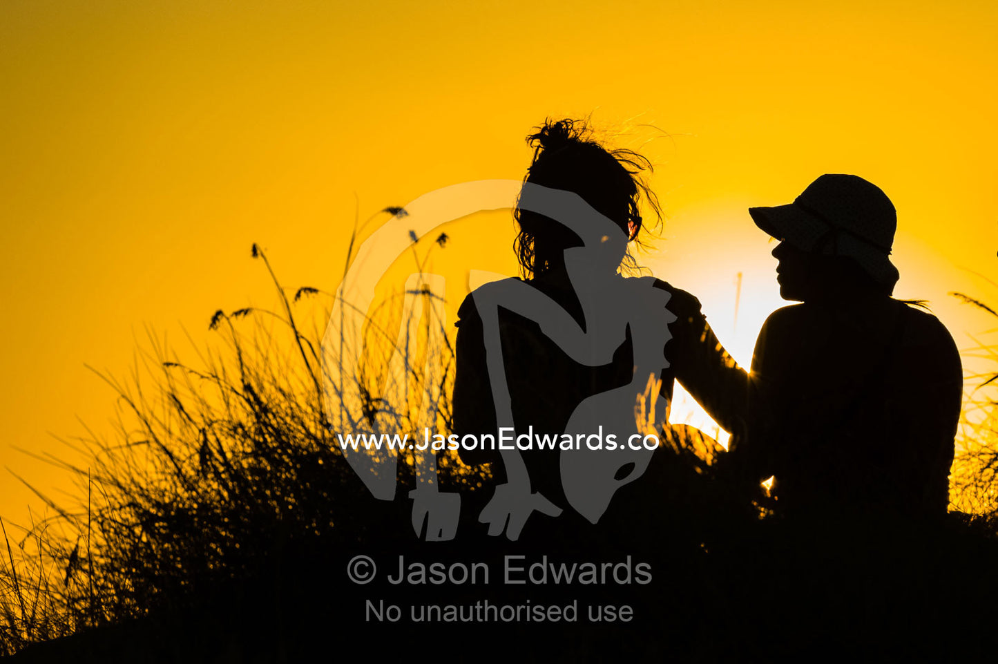 The silhouette of friends watching a famous Top End, sunset from an escarpment over a floodplain. Ubirr, Nadab floodplain, Kakadu National Park, Northern Territory, Australia.