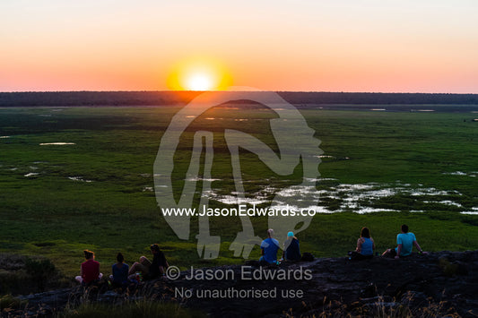 Tourists watch a famous Top End, sunset from an escarpment over a floodplain. Ubirr, Nadab floodplain, Kakadu National Park, Northern Territory, Australia.