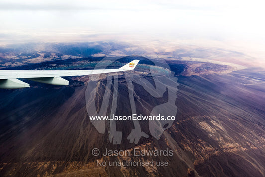 A plane wing passes above the black volcanic slopes of a volcano caldera. Islamic Republic of Iran.