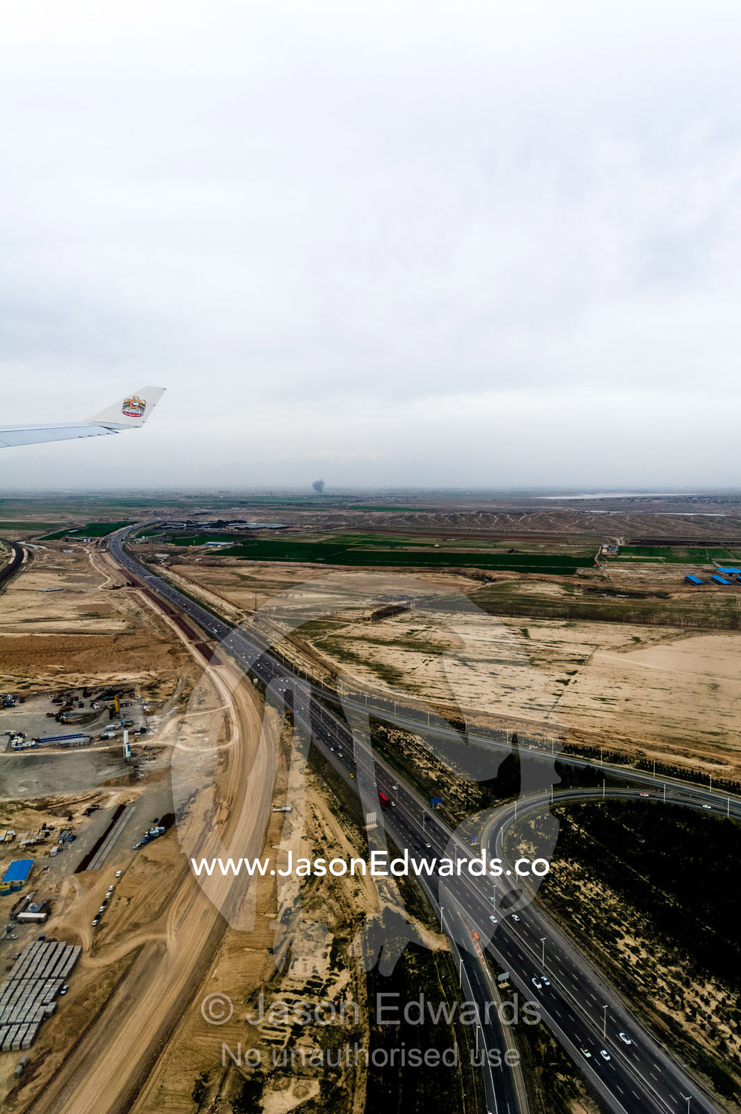 A multi-lane highway crosses a flat plain past a construction site. Tehran, Tehran Province, Islamic Republic of Iran.