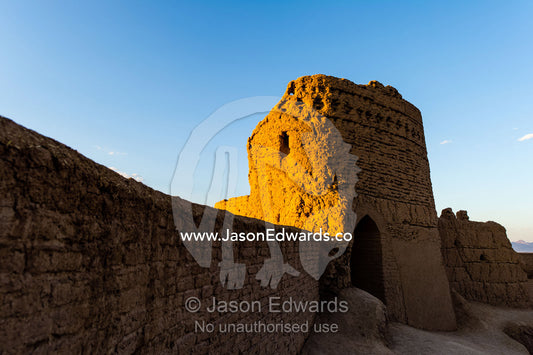 Sunset warms the walls of a watch tower in an ancient mud brick fortress overlooking the desert plain. Narin Castle, Meybod, Meybod County, Yazd Province, Islamic Republic of Iran.