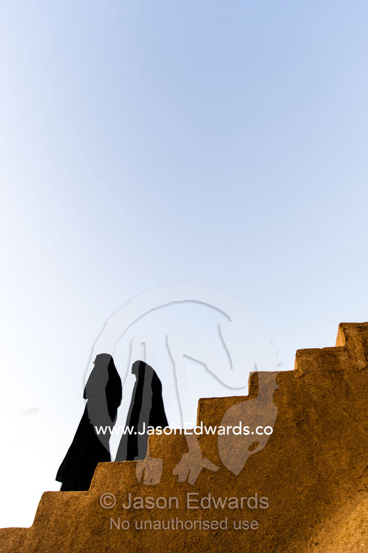 Women dressed in chador descend the stairs of an ancient fortress. Narin Castle, Meybod, Meybod County, Yazd Province, Islamic Republic of Iran.