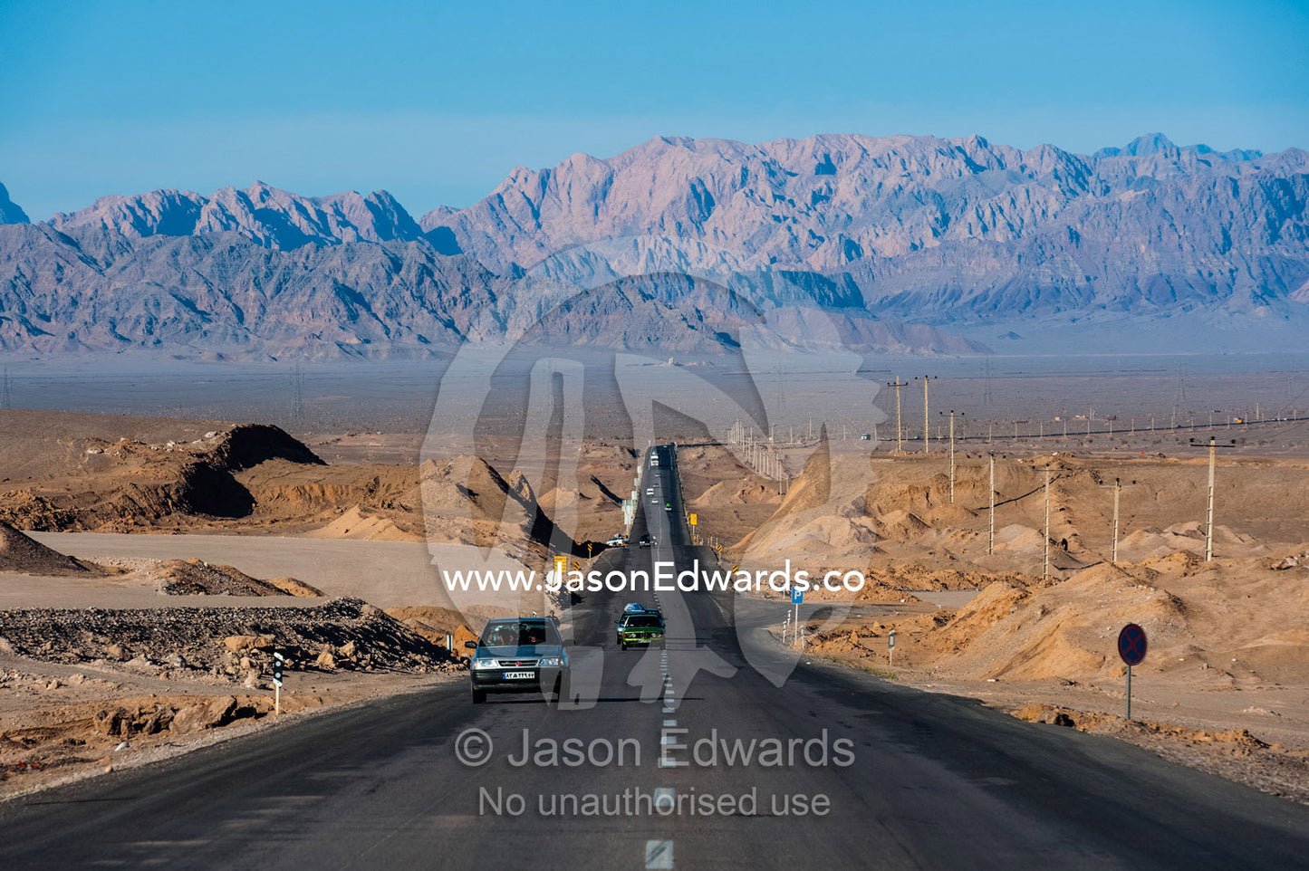 A long straight road crosses the desert towards the mountains. Kharanagh, Yazd, Yazd Province, Islamic Republic of Iran.