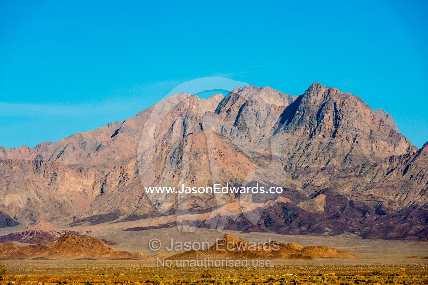 Erosion on the slopes of jagged desert mountain peaks beneath a clear blue sky. Kharanagh, Yazd, Yazd Province, Islamic Republic of Iran.