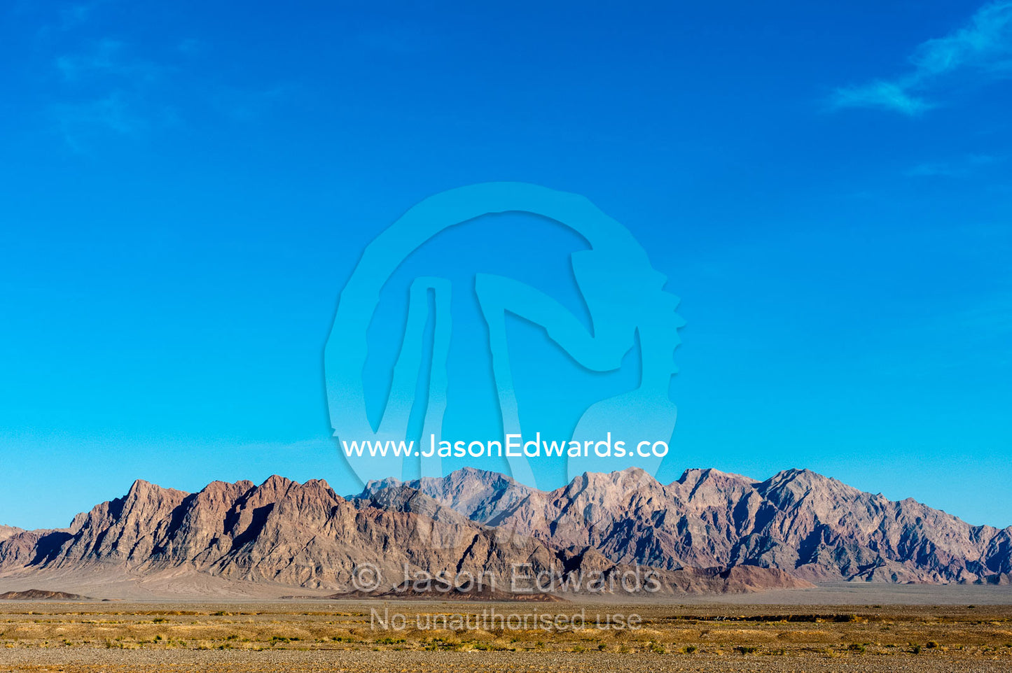 Erosion on the slopes of jagged desert mountain peaks beneath a clear blue sky. Kharanagh, Yazd, Yazd Province, Islamic Republic of Iran.