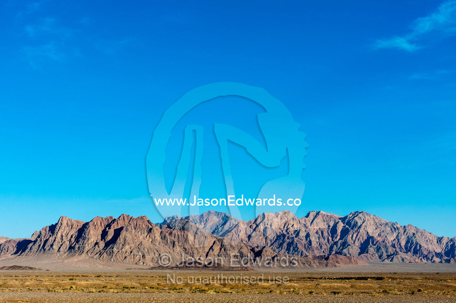 Erosion on the slopes of jagged desert mountain peaks beneath a clear blue sky. Kharanagh, Yazd, Yazd Province, Islamic Republic of Iran.