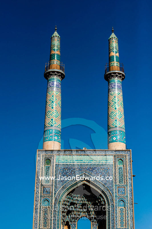 The towering blue tiled minarets above the vaulted iwan of the Jame Mosque rise into a clear blue sky. Jame Mosque of Yazd, Yazd, Yazd Province, Islamic Republic of Iran.