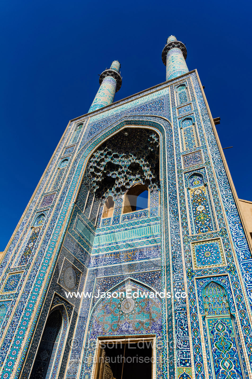 The towering blue tiled minarets above the vaulted iwan of the Jame Mosque rise into a clear blue sky. Jame Mosque of Yazd, Yazd, Yazd Province, Islamic Republic of Iran.