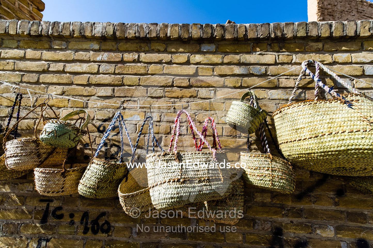Hand woven grass bags for sale on a brick wall. Yazd, Yazd Province, Islamic Republic of Iran.