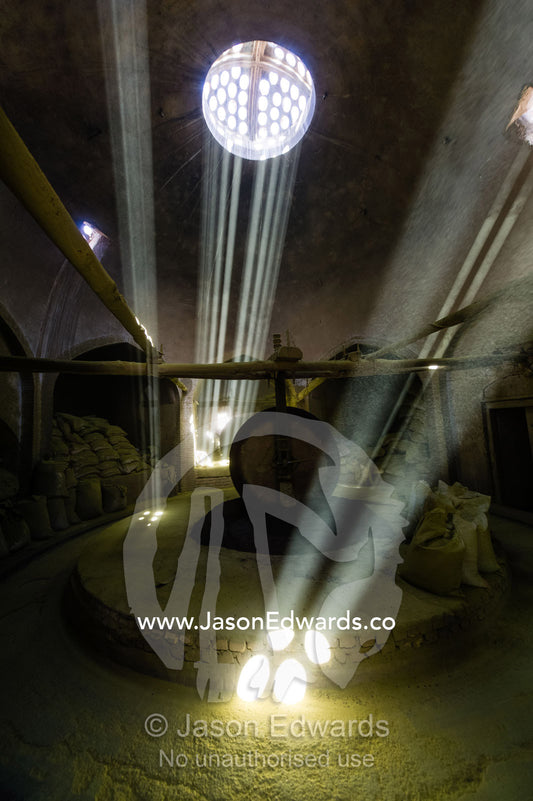 Sunrays light a giant stone wheel grinding henna seeds into powder in an ancient henna mill. Yazd, Yazd Province, Islamic Republic of Iran.