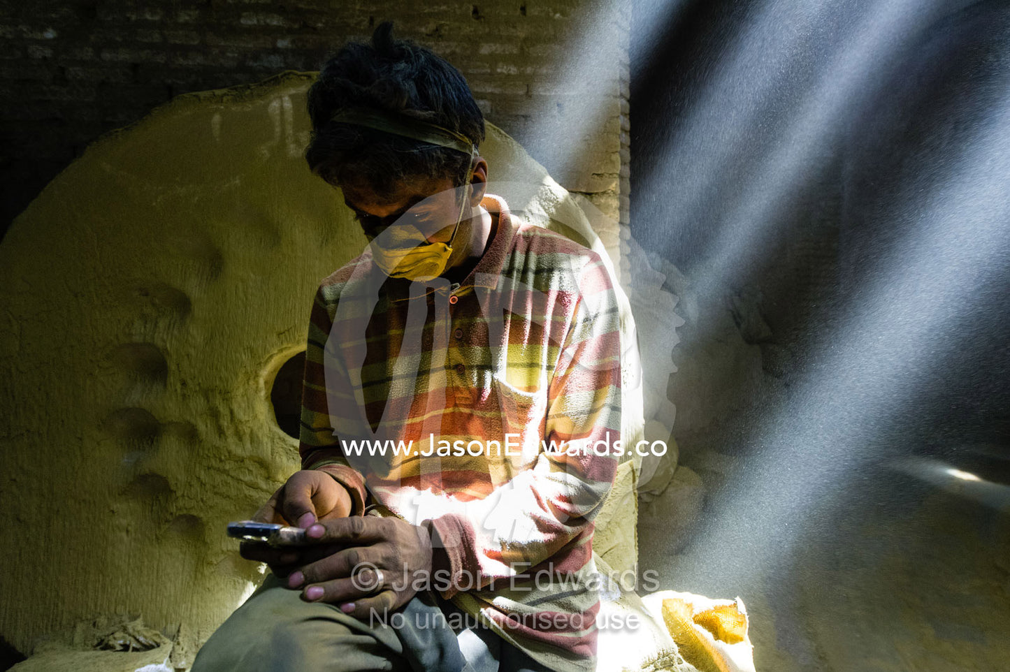 A labourer wearing a dust mask sends a text message on a cell phone in an ancient henna mill. Yazd, Yazd Province, Islamic Republic of Iran.