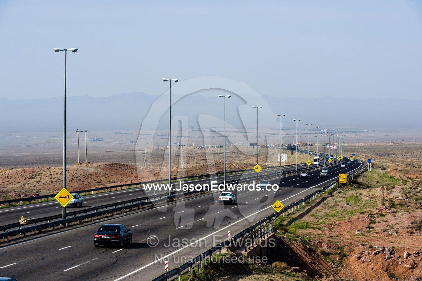 Traffic moves along a multi-lane highway crosses a flat plain in the desert. Qom Province, Islamic Republic of Iran.