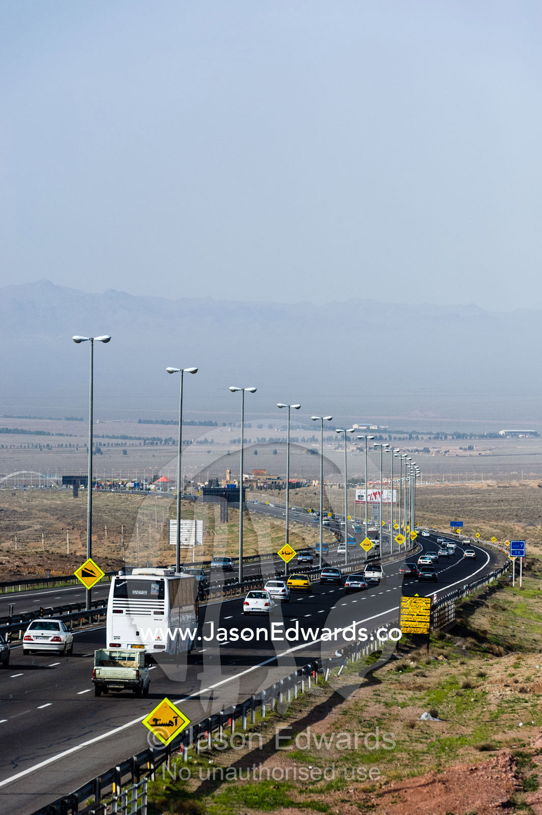 Traffic moves along a multi-lane highway crosses a flat plain in the desert. Qom Province, Islamic Republic of Iran.