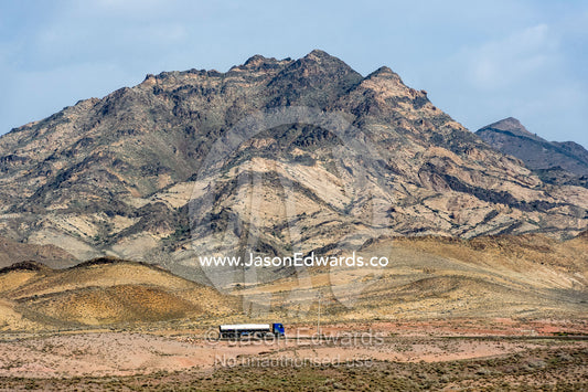 A tanker truck travels through the desert beneath jagged peaks. Qom Province, Islamic Republic of Iran.